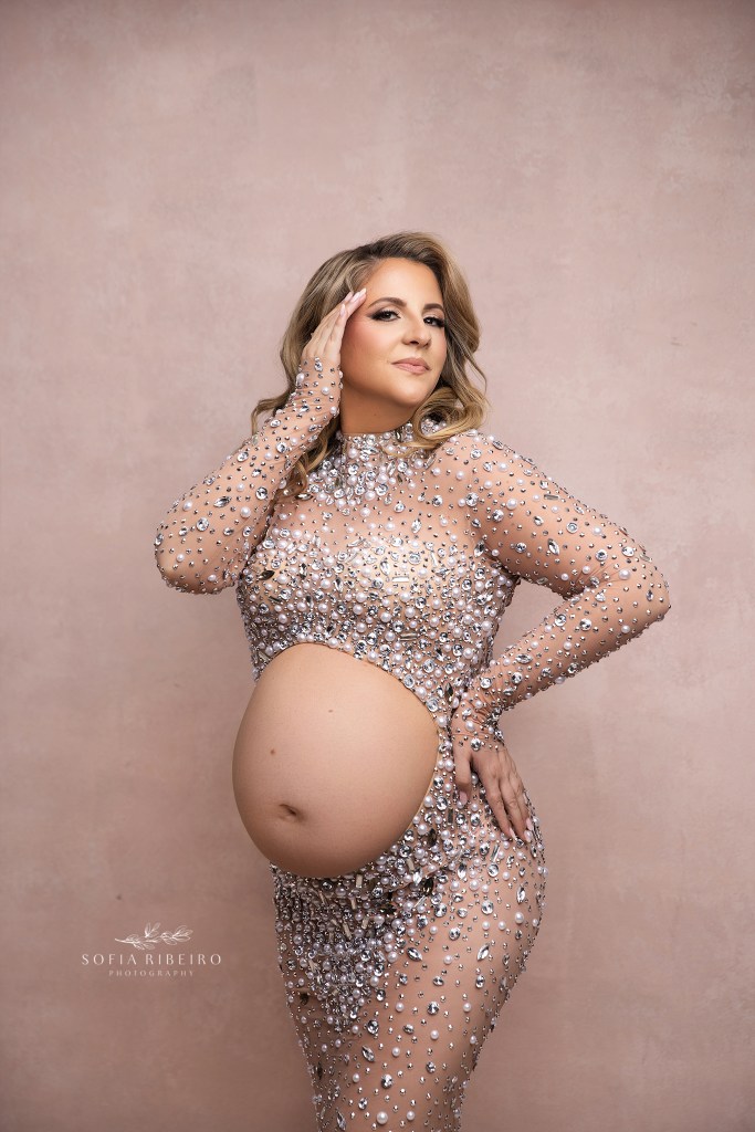 mom poses with her belly exposed in a rhinestone gown, hand to temple in a powerful pose, in a portrait created by a middletown nj maternity photographer