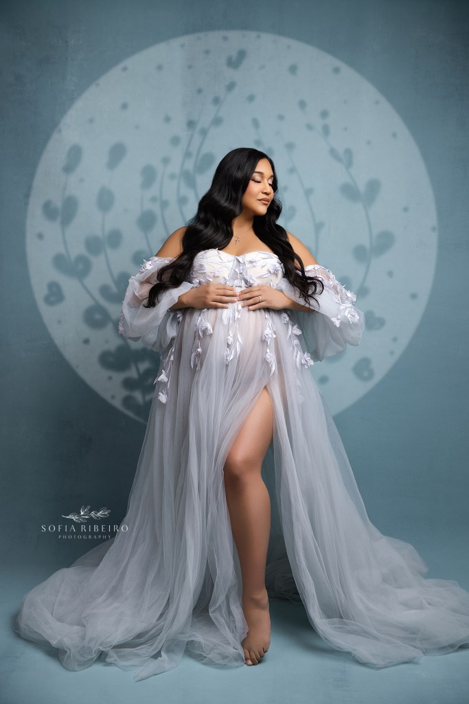mom to be frames her baby bump against a blue backdrop with a blue tulle gown for a portrait in a nutley nj maternity photography studio