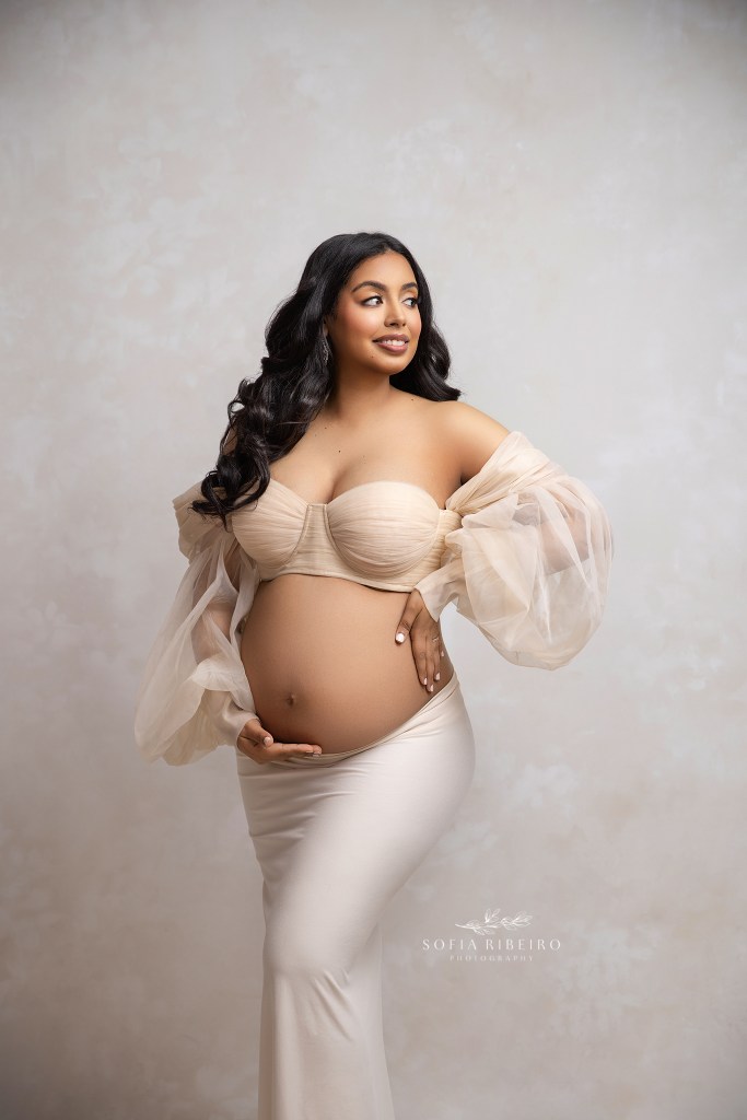 mom to be in passaic nj in a two piece beige outfit exposing her baby bump and smiling off camera