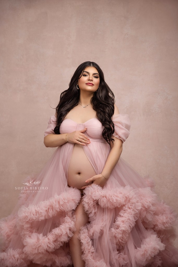 mom to be is the picture of serenity in a pink ruffled gown exposing her belly.