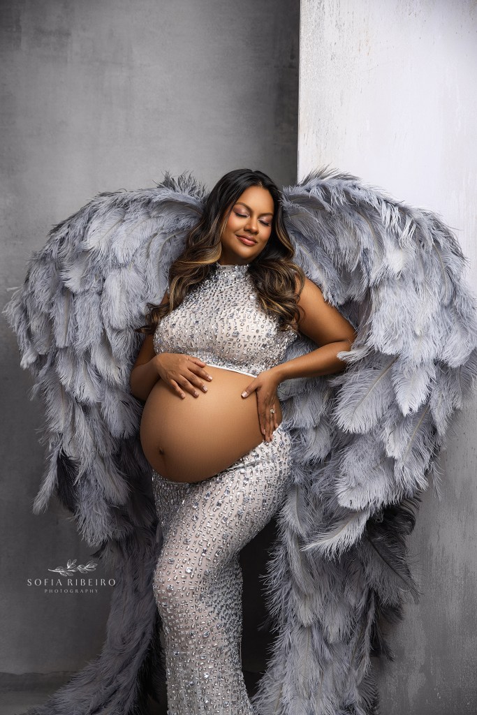 a franklin lakes nj maternity photographer frames mom to be in angel wings in a stunning silver jeweled two piece look exposing her baby bump