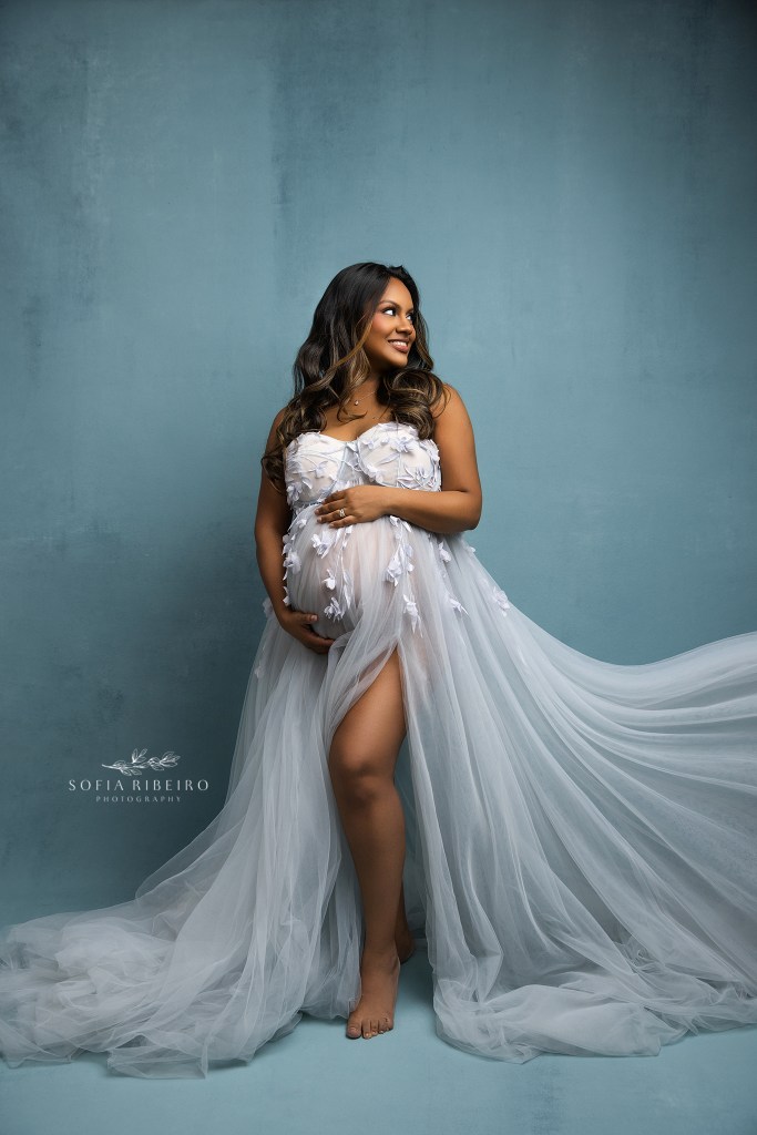 a radiant mom to be in blue poses in blue for maternity portraits in franklin lakes