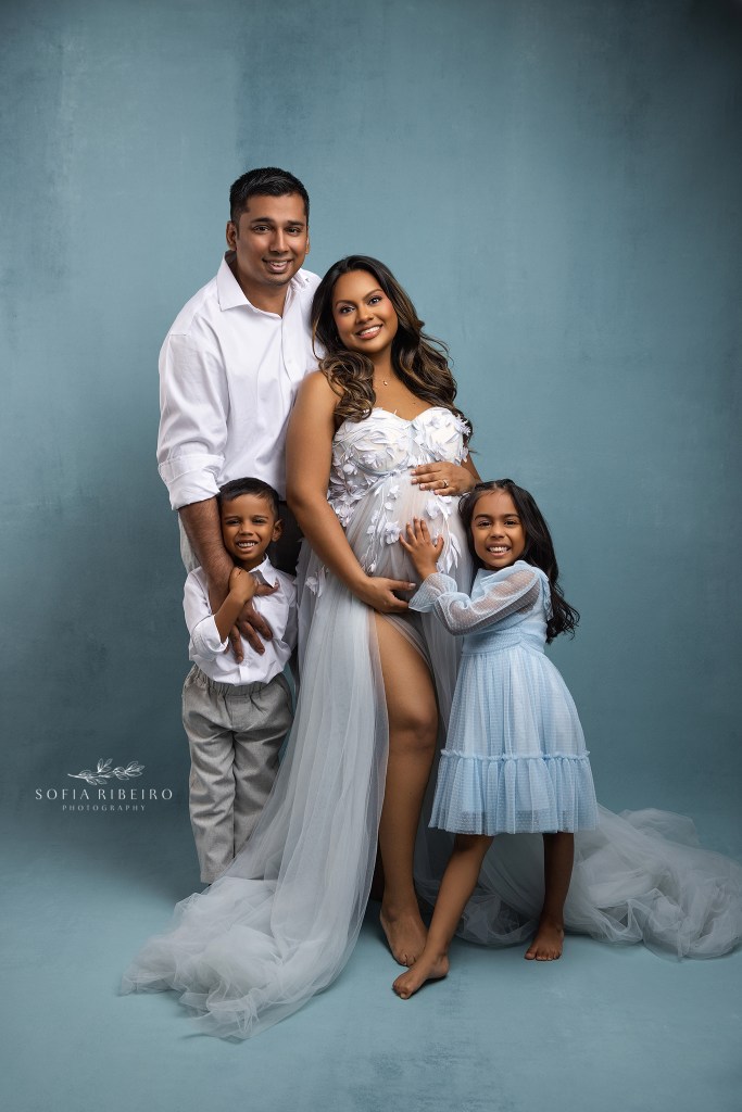 a family of four expecting a new baby pose for a charming family portrait in shades of blue