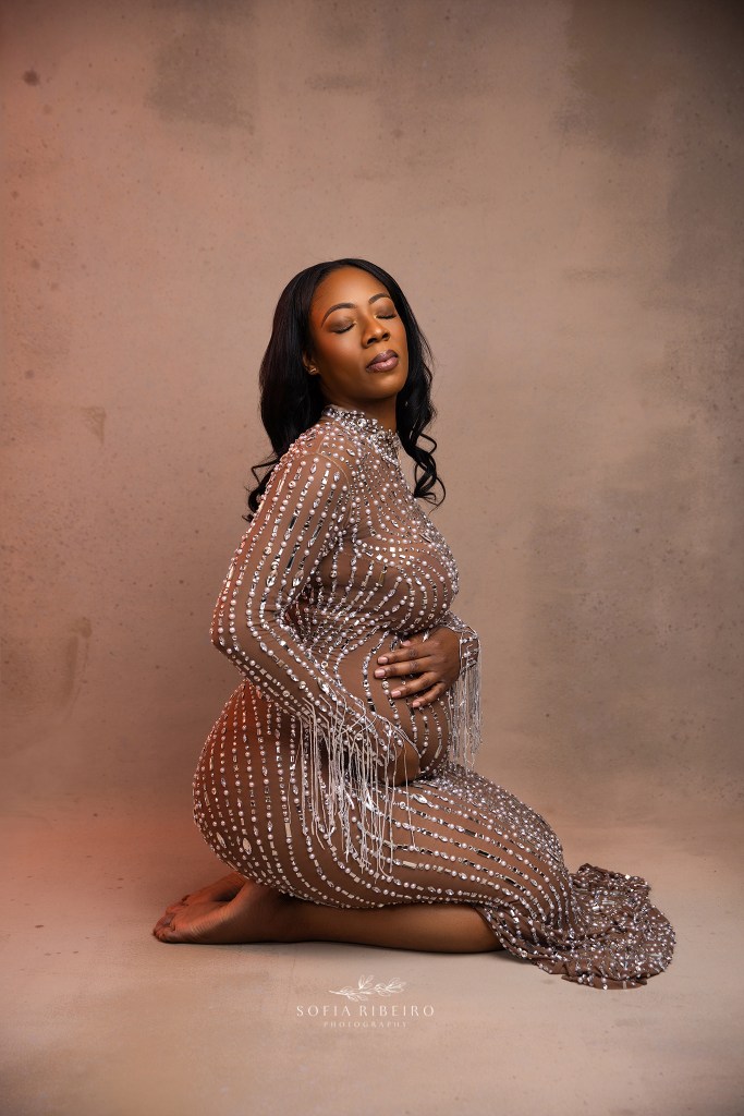 an allover rhinestone gown enhances moms baby bump in a seated portrait framing the belly