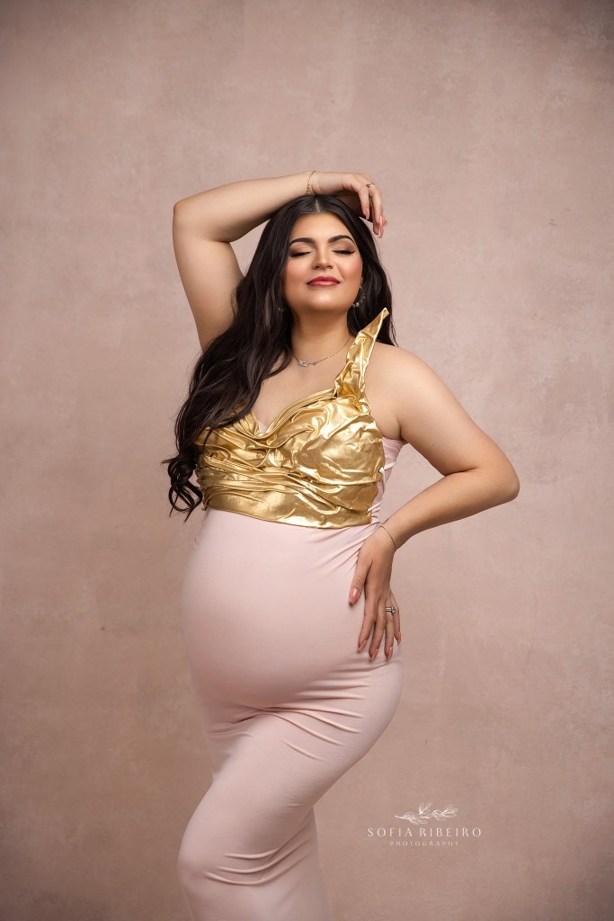 mom to be poses with her arm above her head, and one on her waist, emphasizing her growing bump