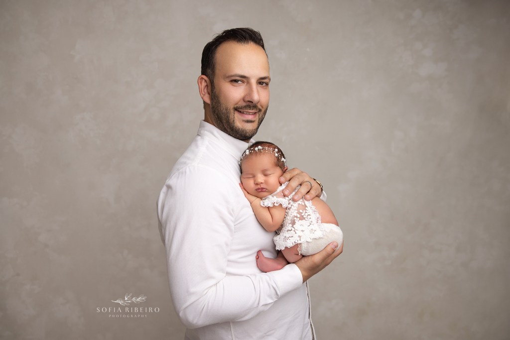 dad proudly poses with his newborn baby girl for a portrait