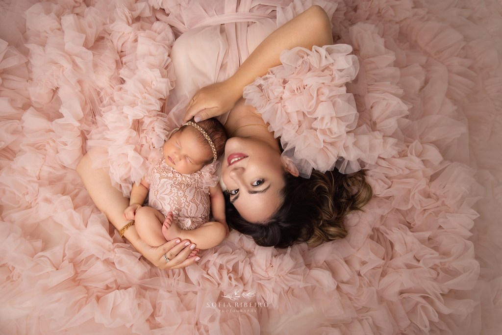 mom is posed with baby in a lie down position on the floor in a pink tulle gown in maplewood nj