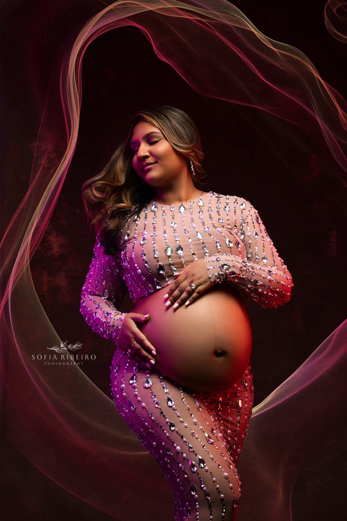 expectant mom swishes her hair around in an artful maternity portrait with a two piece gemstone outfit and gel lighting