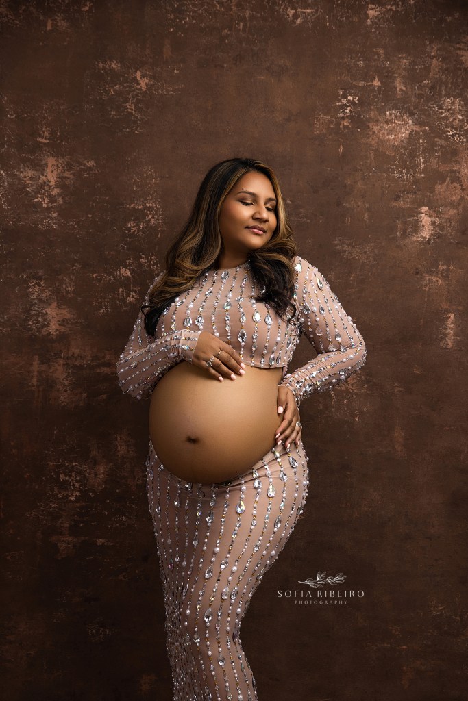 mom poses with hands creating triangles surrounding her belly in a two piece rhinestone outfit
