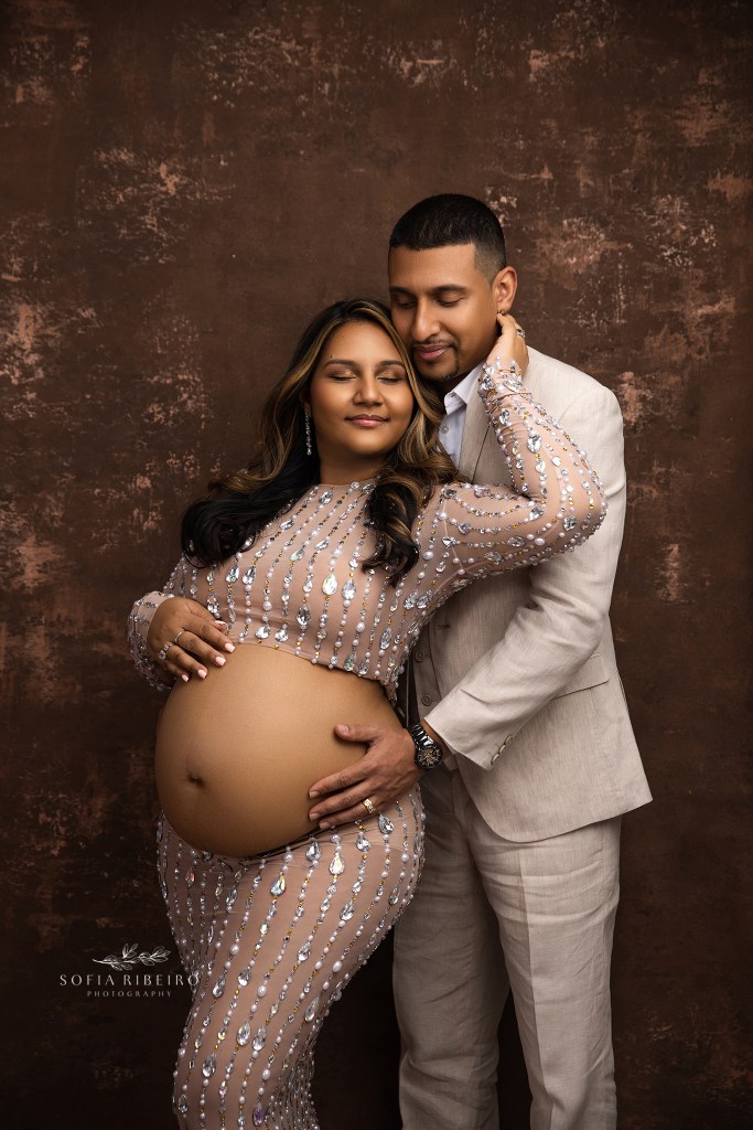 mom and dad share a sweet moment in netural tones against a brown and gold backdrop for maternity photos