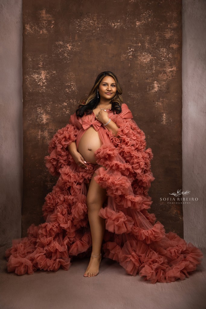 mom to be poses in a coral gown with baby bump exposed in an elegant maternity portrait