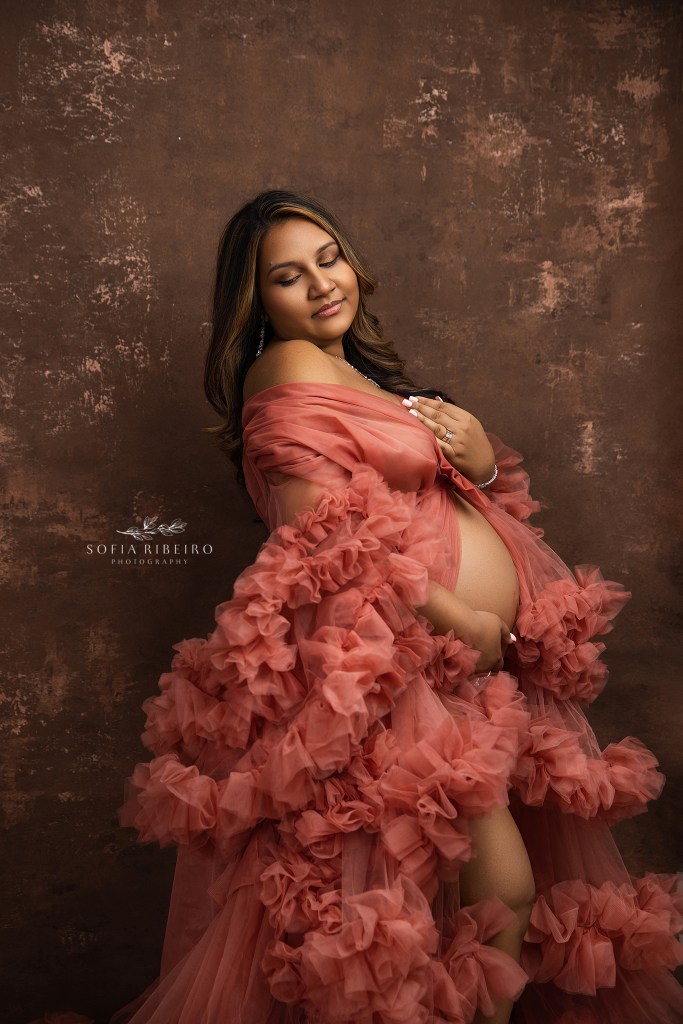 an expectant mom cradles her belly in a coral tulle gown for a maternity portrait in a new brunswick nj maternity photographer's studio