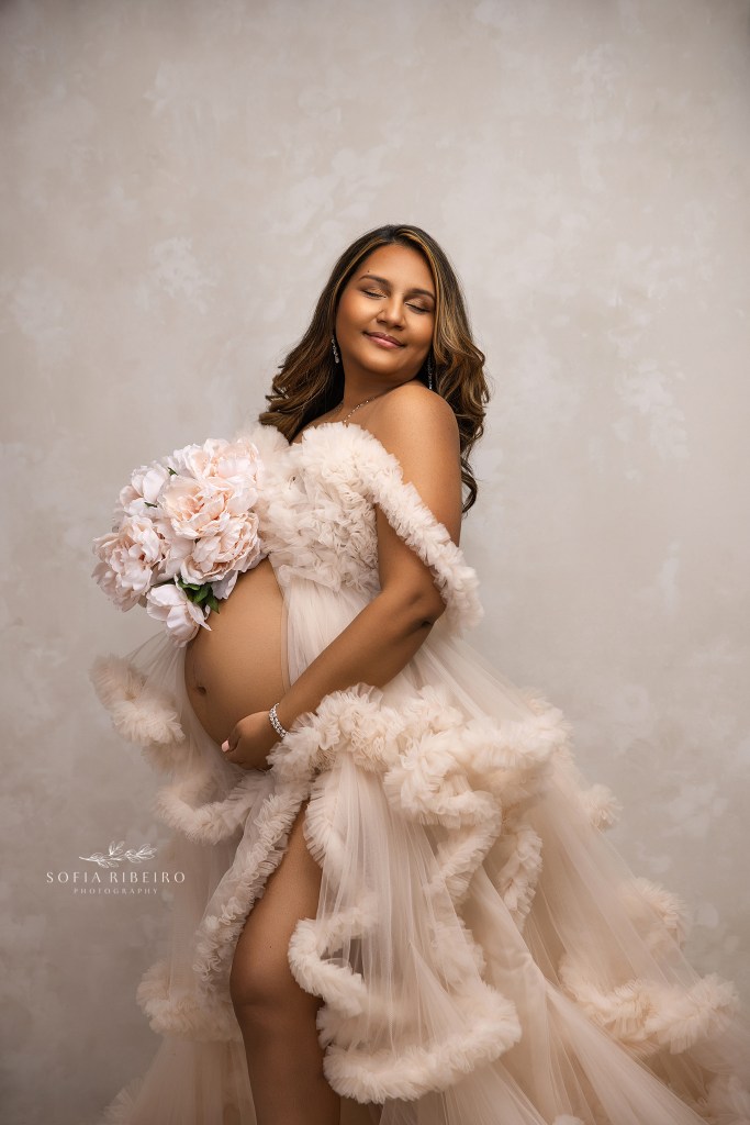 mom poses cradling her baby bump and a bouquet of flowers for a maternity photo