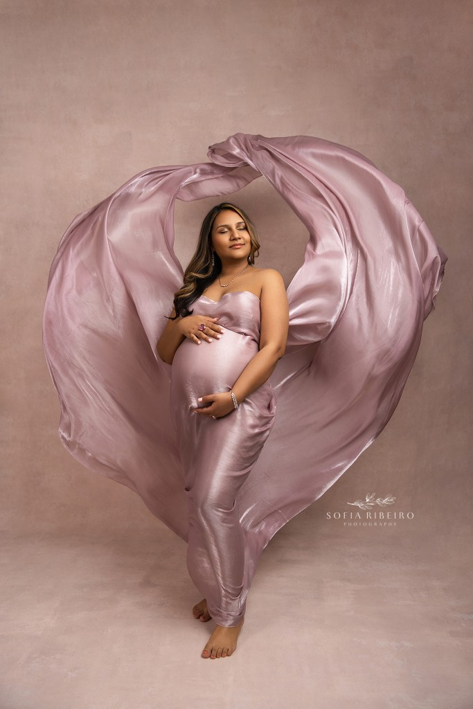 north brunswick nj maternity photographer poses a mom in blush toned fabric against a pink backdrop