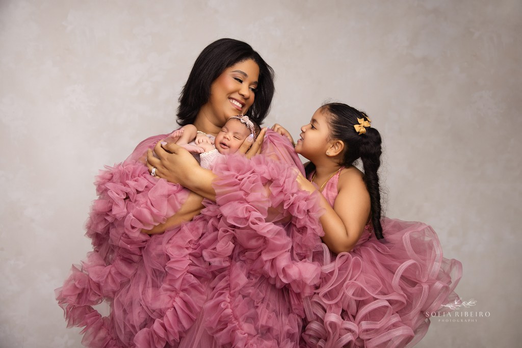 mom smiles to her older daughter in matching pink outfits while holding her newborn baby girl