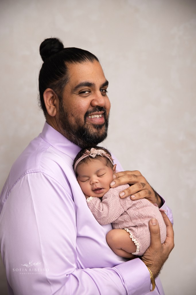 dad smiles to camera with his newborn baby girl matching his smile