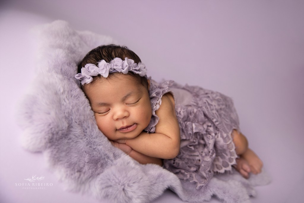 newborn baby girl is posed in a lavender color scheme and outfit
