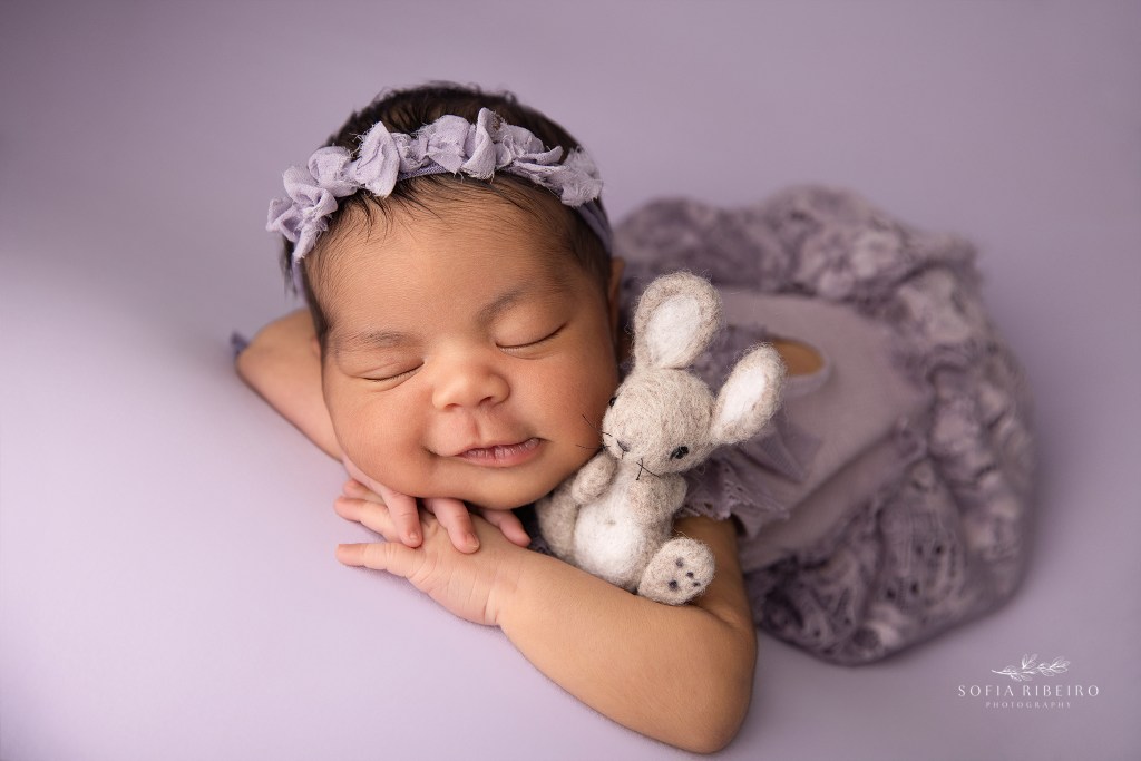 sussex nj newborn photographer captures a baby girl smiling in purple outfit and backdrop with a teddy