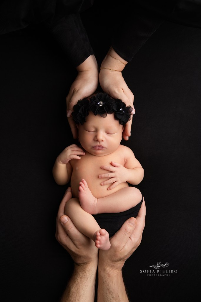 holmdel nj newborn photographer poses baby in an all black setup with parent's hands on baby