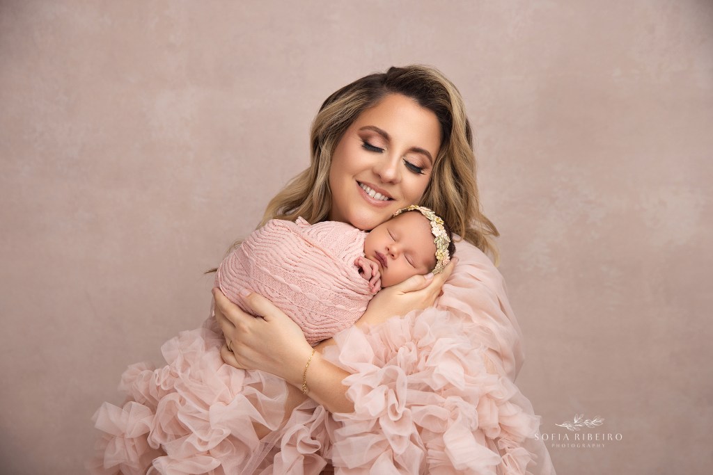 mom snuggles her baby daughter in a pink dress and wrap for newborn photos