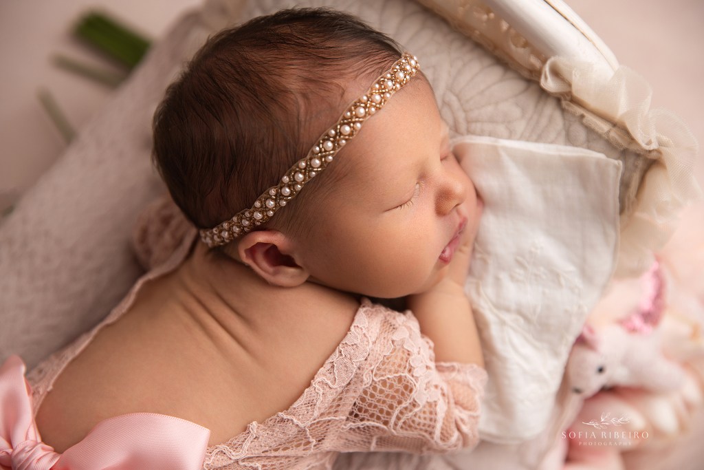 a closeup of a side profile of a newborn baby girl in a pearl headband and lace bodysuit