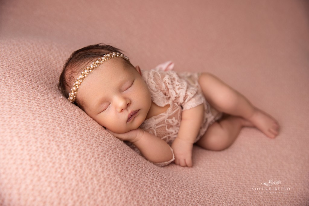 a holmdel nj newborn photographer poses baby in a side lying pose against a pink backdrop