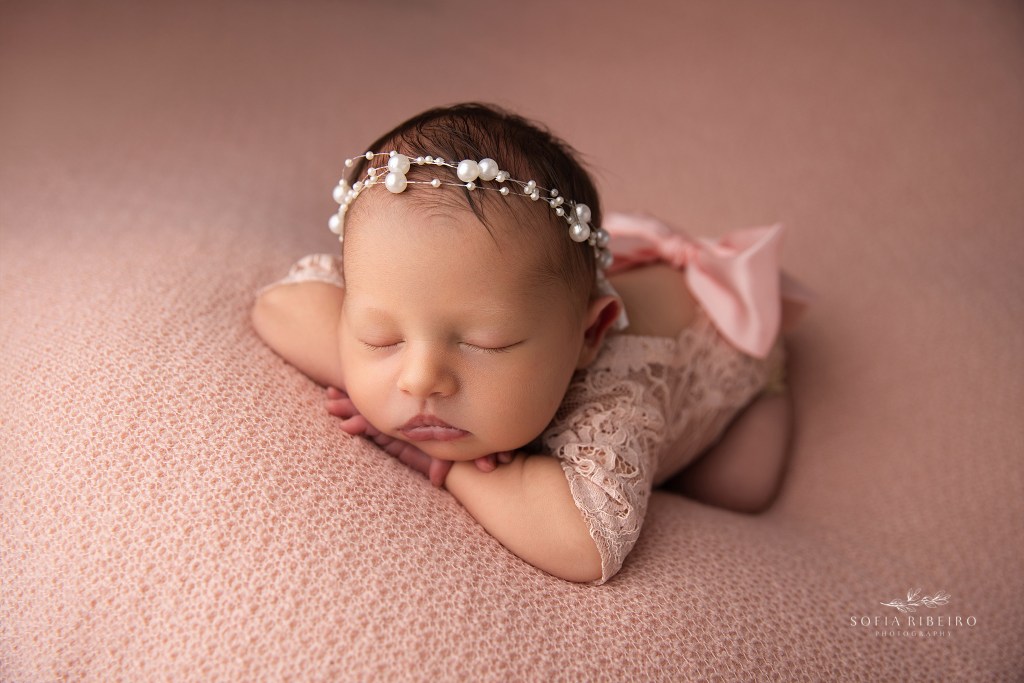 baby is posed head on hands in a pearl headband for newborn portraits in nj