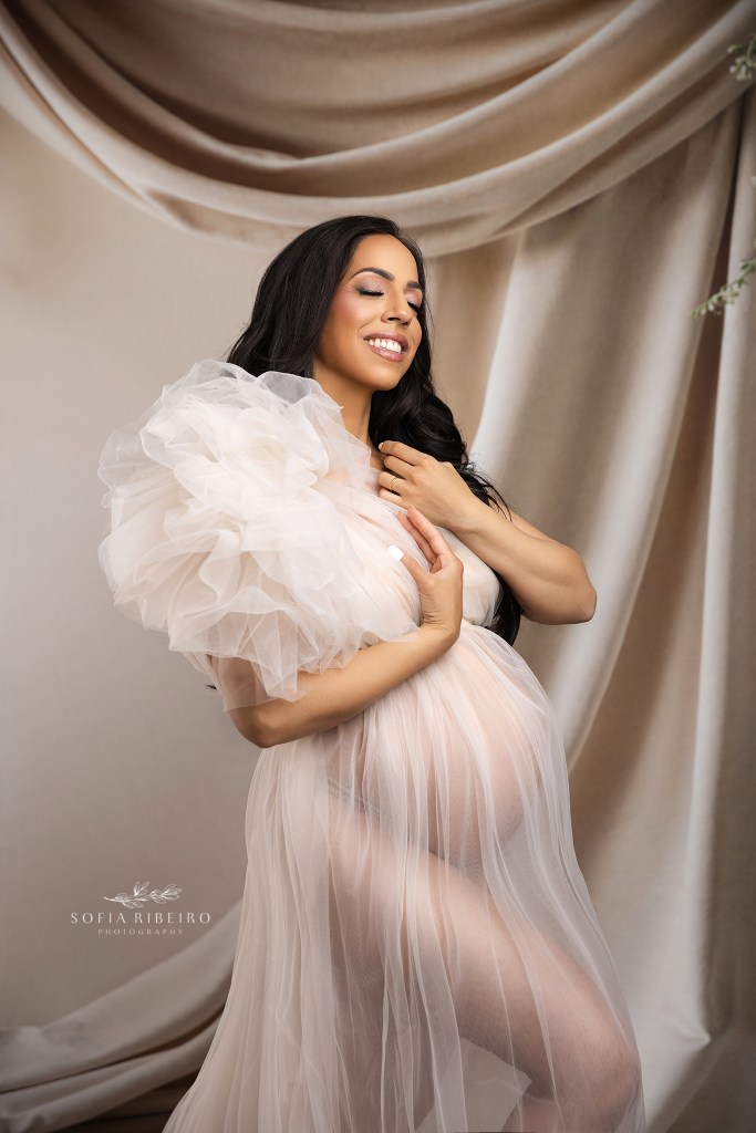 mom shows of her growing bump in a layer o cream tulle for a maternity portrait in new york city
