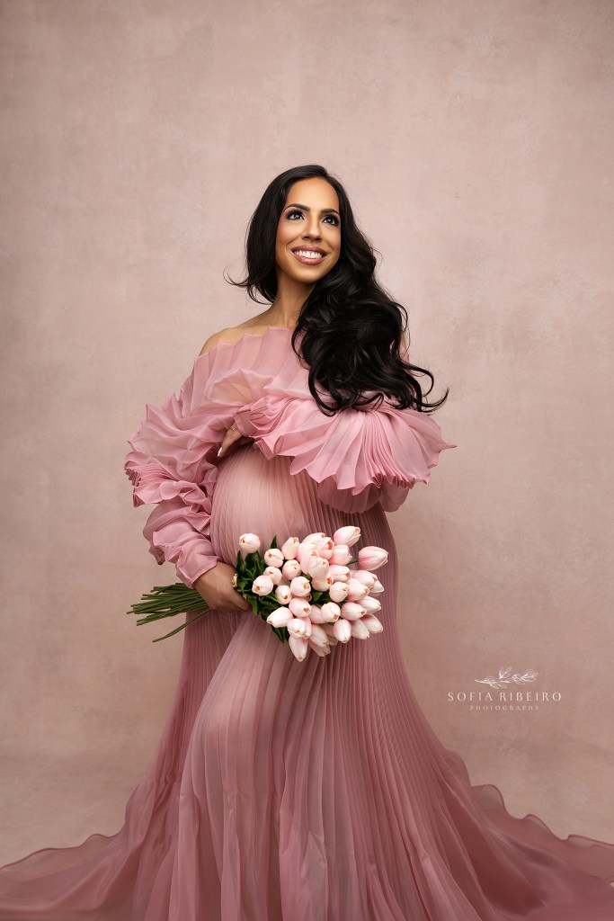 a soft pink pleated gown is framed with pink tulip in moms smiling maternity portrait