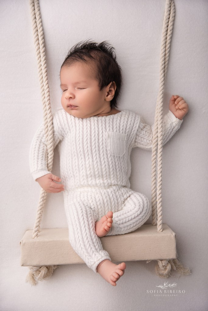 Sleepy newborn in a tiny swing prop captured at an Essex County NJ photography studio.