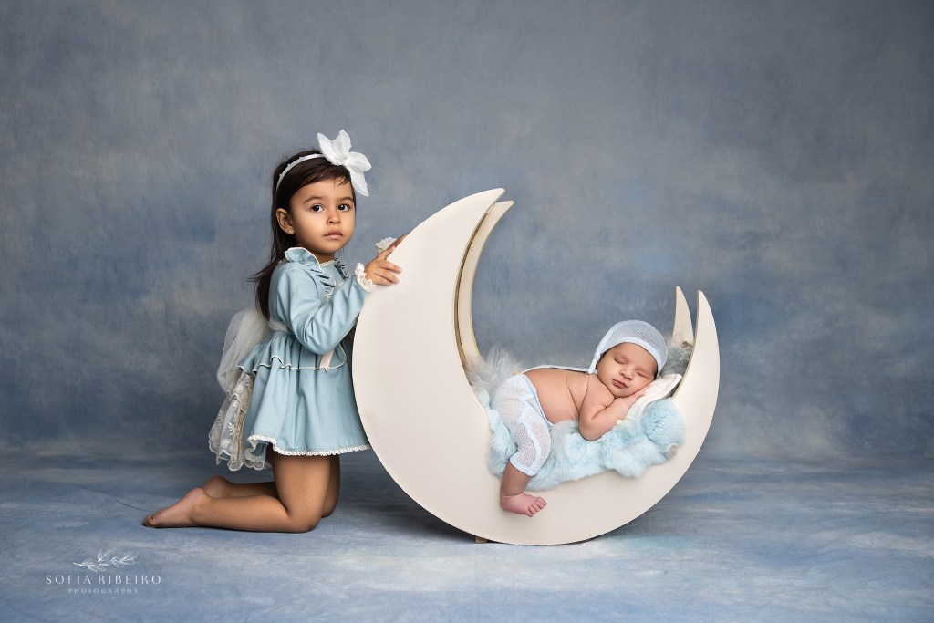 Newborn session with big sister posing in a moon prop, captured in Essex County NJ.