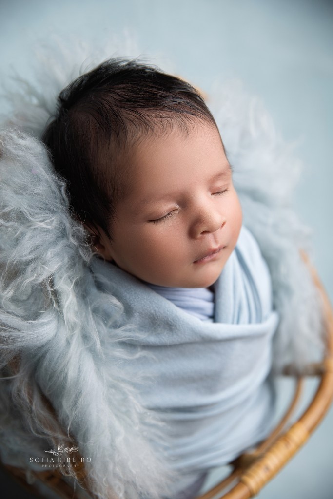 Serene newborn baby wrapped in blue, sleeping soundly in studio light.
