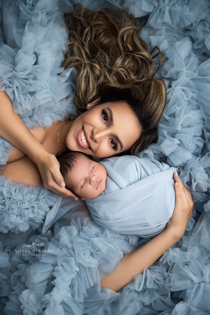 mom beams with pride, cradling her newborn baby boy in soft blue tones on a bed of tulle