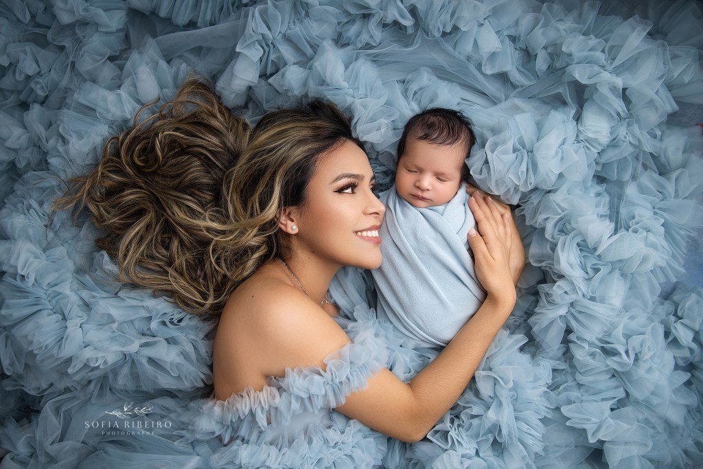 mom and baby pose together in a lie down pose in a bed of blue tulle ruffle in an essex county nj newborn photography studio