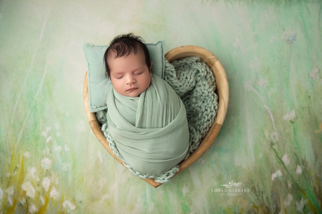 Essex County NJ newborn photography session with baby boy swaddled in sage green tones in a wooden heart prop