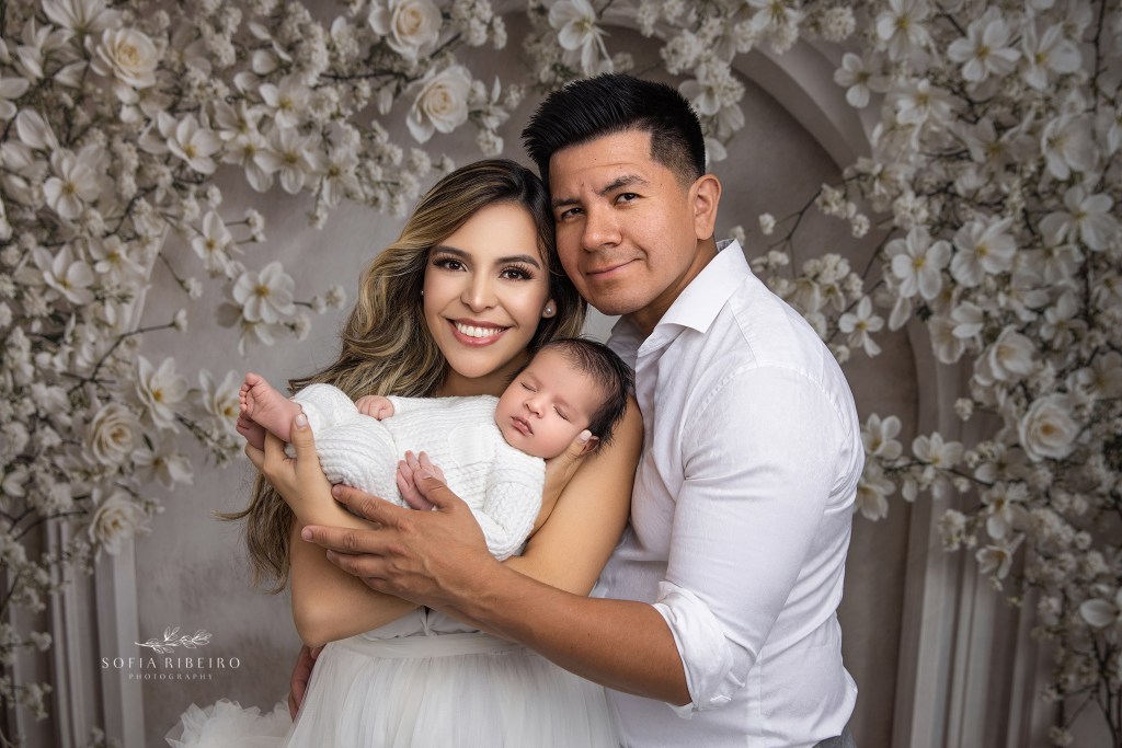 mom and dad smile to camera while holding their newborn baby boy