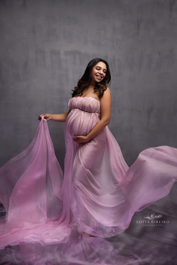 an expectant mom cradles her belly with flowing fabric around her in pink