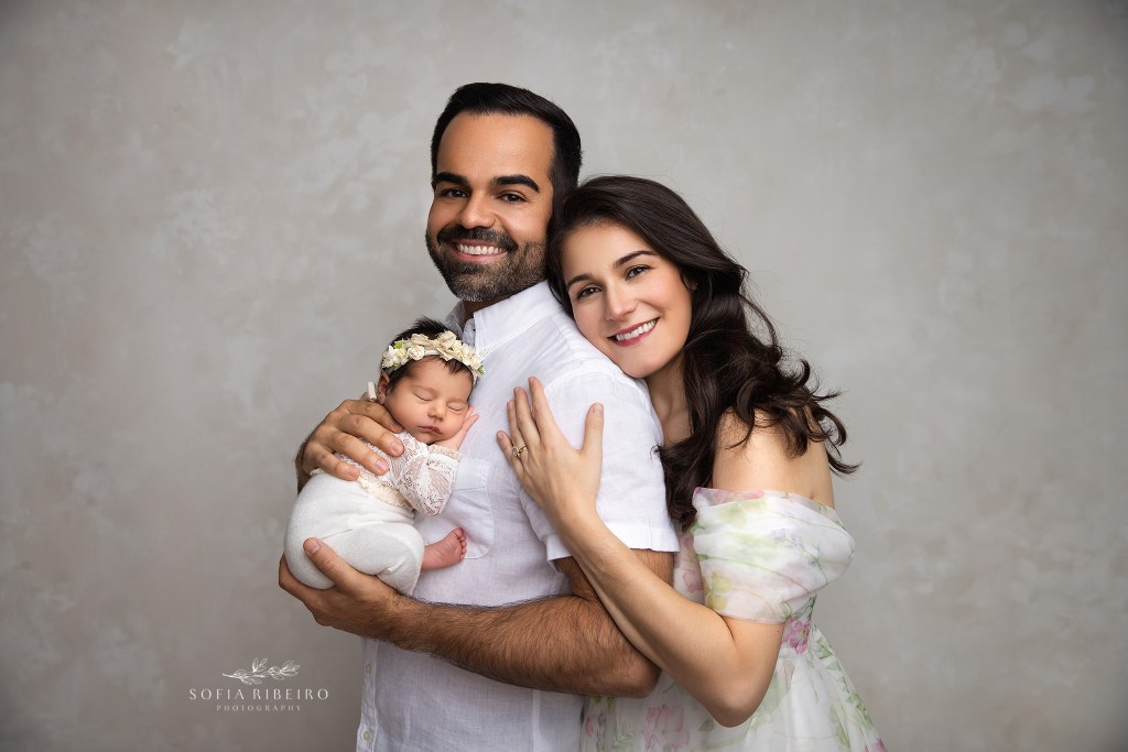 mom and dad smile sweetly to camera while holding their new little one