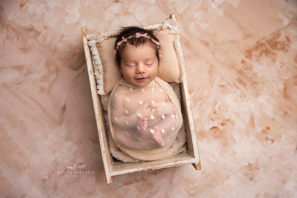 nj newborn photographer captures Baby girl sleeping peacefully in a sheer wrap, surrounded by a soft floral backdrop