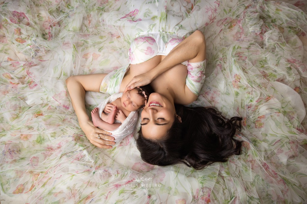 Mother cradling her baby girl in flowing fabrics with soft pink accents.