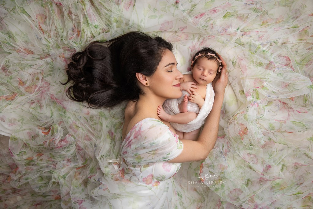 Mother cradling her baby girl in flowing fabrics with soft pink accents.