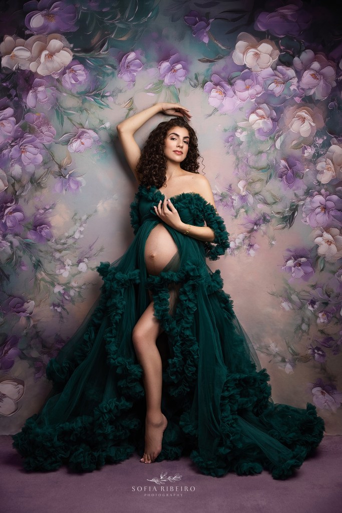 a pregnant mom is radiant in an emerald green gown with bump exposed against a floral backdrop