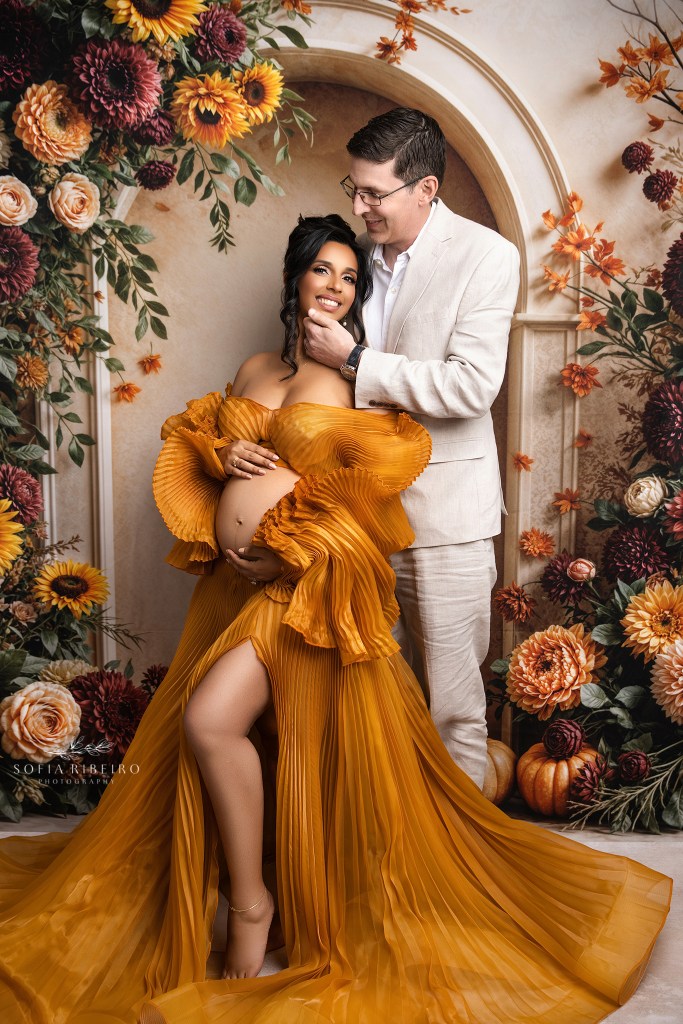 Dad cradles moms face lovingly during a maternity session set against a fall backdrop