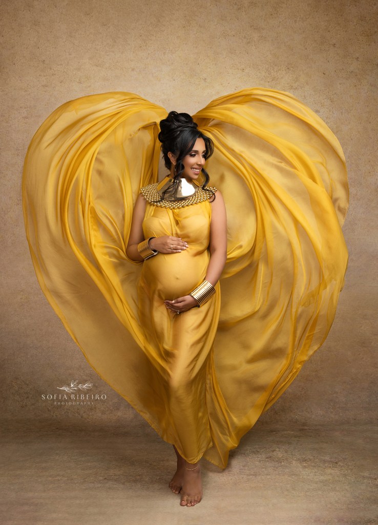 Expecting mother in a flowing yellow fabric against neutral tones at a studio in Princeton.