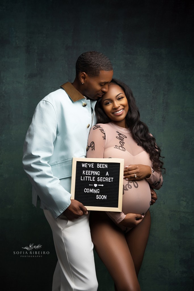 parents to be pose with a sign announcing their pregnancy during a maternity photoshoot