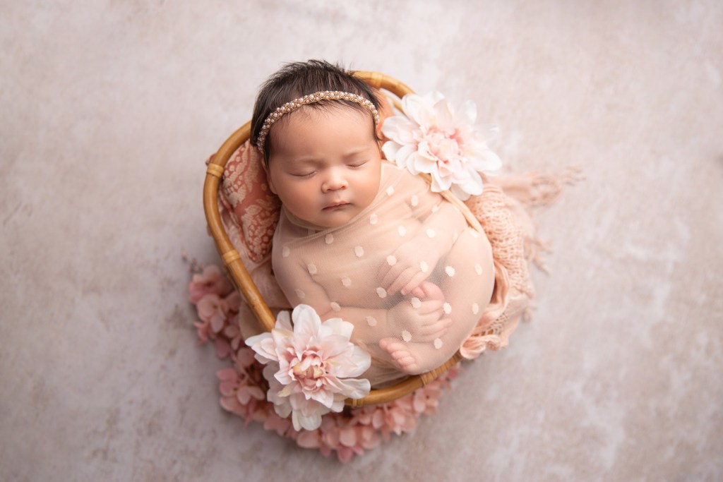 baby girl in pink basket w flowers in nj newborn photographer's studio