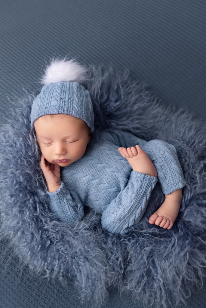 a newborn baby boy is posed in blue during a portrait session in a photography studio in nj