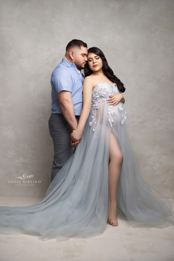 a couple shares a tender moment while cradling the baby bump in soft blue and cream hues