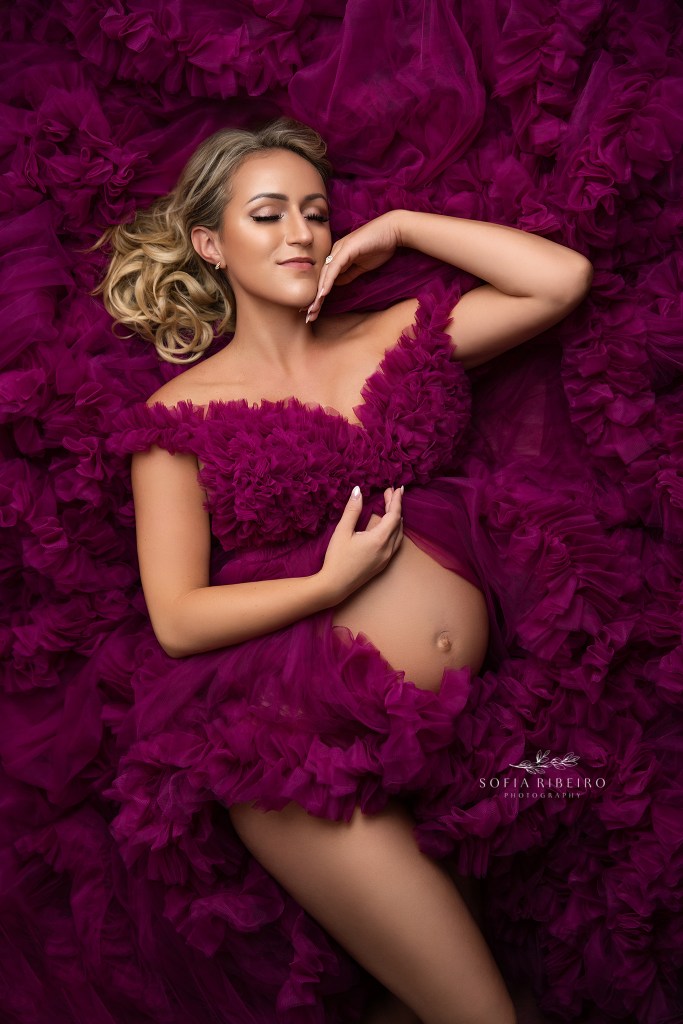 mom is shot in a side lying pose in a magenta ruffle dress exposing her baby bump