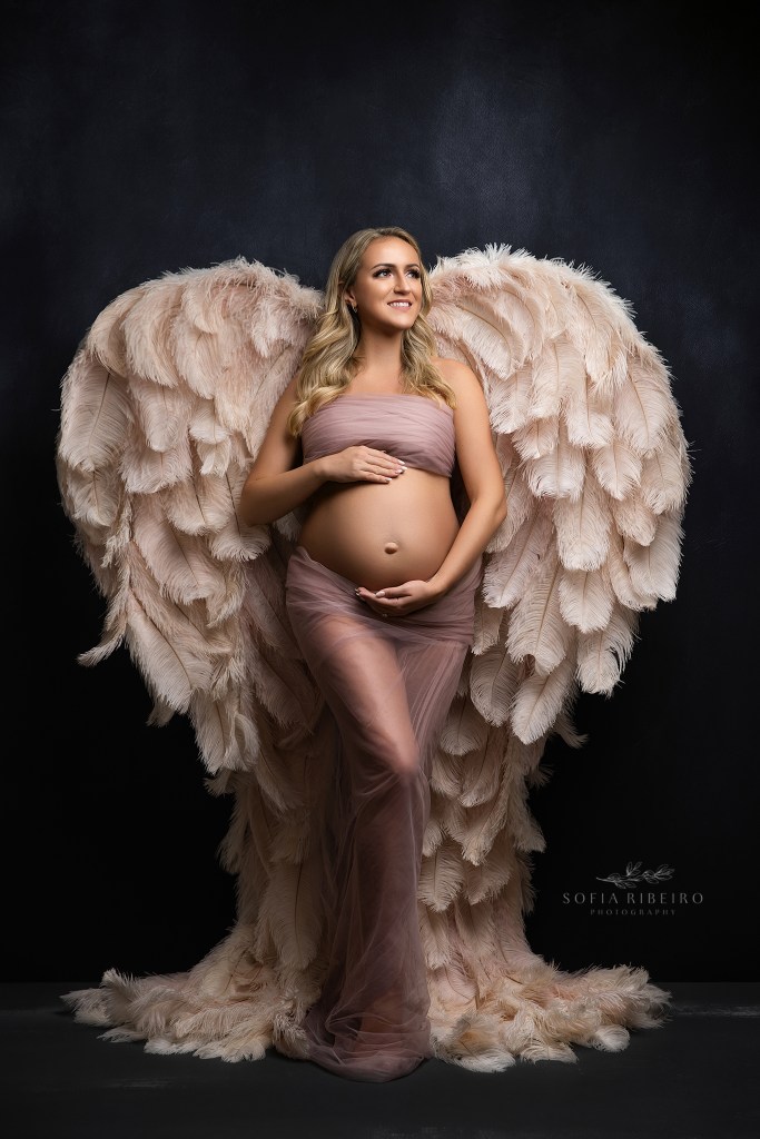 ridgewood nj maternity photographer poses moms to be against dramatic backdrop, here with angel wings and sheer tulle